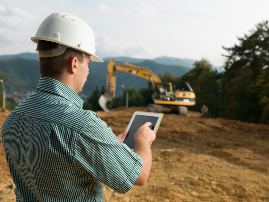 back view of caucasian engineer standing on construction site checking plan on digital tablet